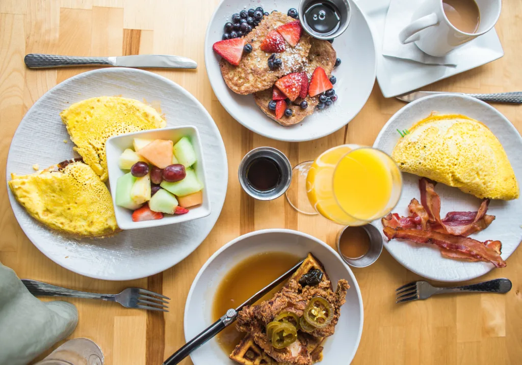 A balanced breakfast of eggs, fruit, bacon, and whole grains sits on a table. This meal is recommended by nutritional therapists though you may not have an appetite in the morning 