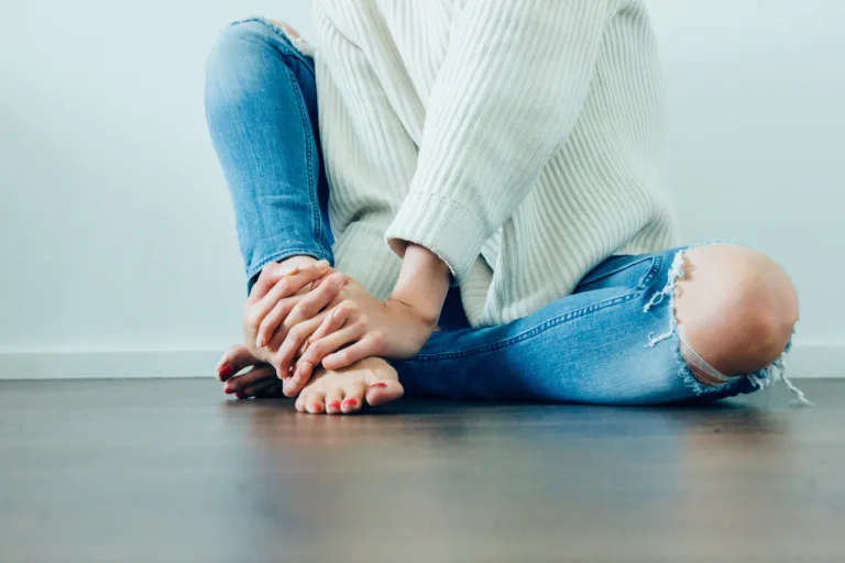 Woman with thyroid and period problems sits on the ground hands grasping her feet