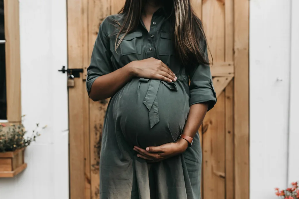 A pregnant women in a green dress holds her belly facing the camera. You can't see her face. She experienced light periods that were actually related to her pregnancy not true periods 