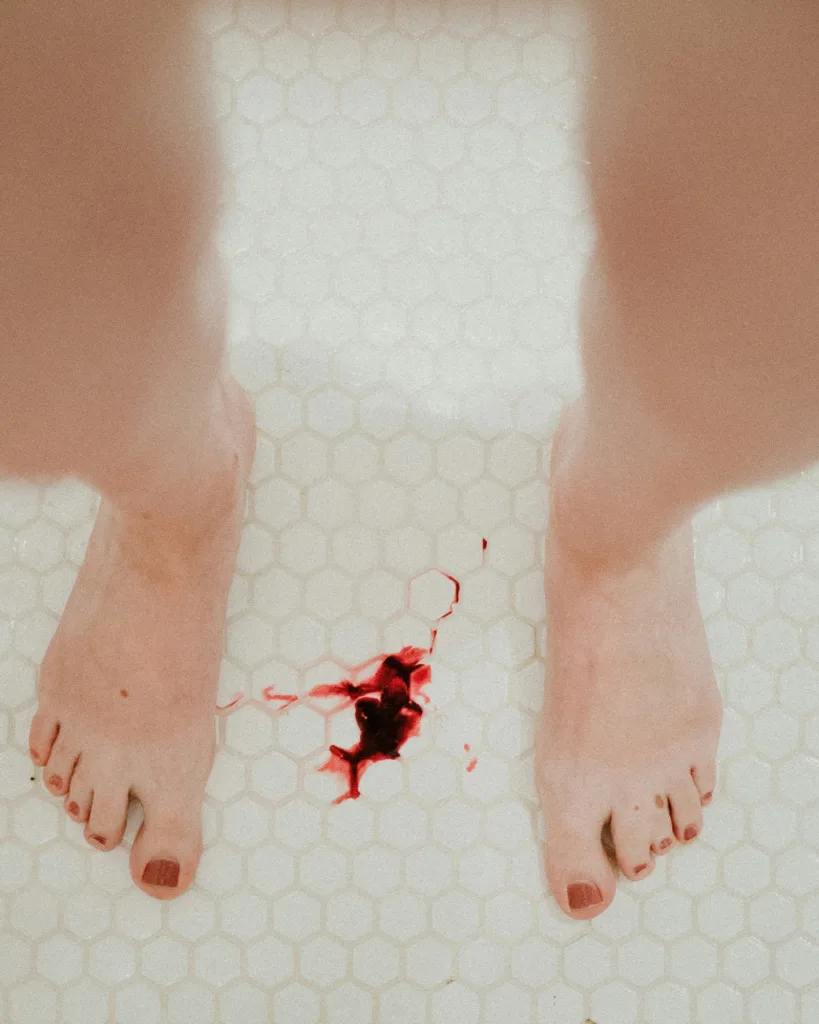 blood is on the bathroom floor between a woman's bare feet because of a heavy period 