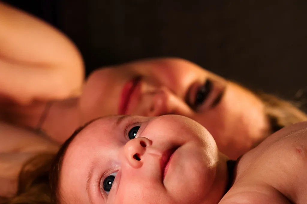 A mother and baby lay head to head. The baby is in the foreground looking up and the mother is in the background looking at the baby 