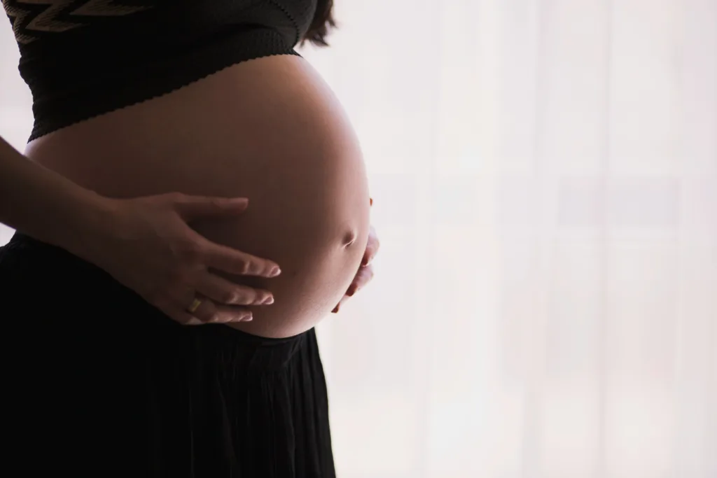 A close-up photo of a pregnant woman's belly with her hands holding her belly.