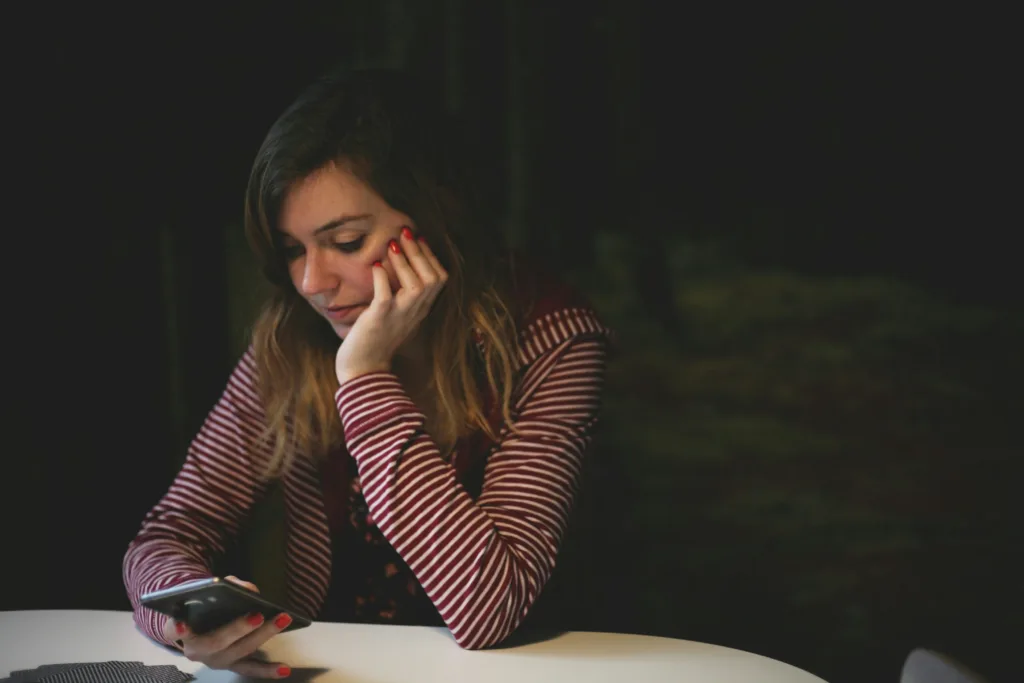 A woman with concern on her face is looking down at her phone