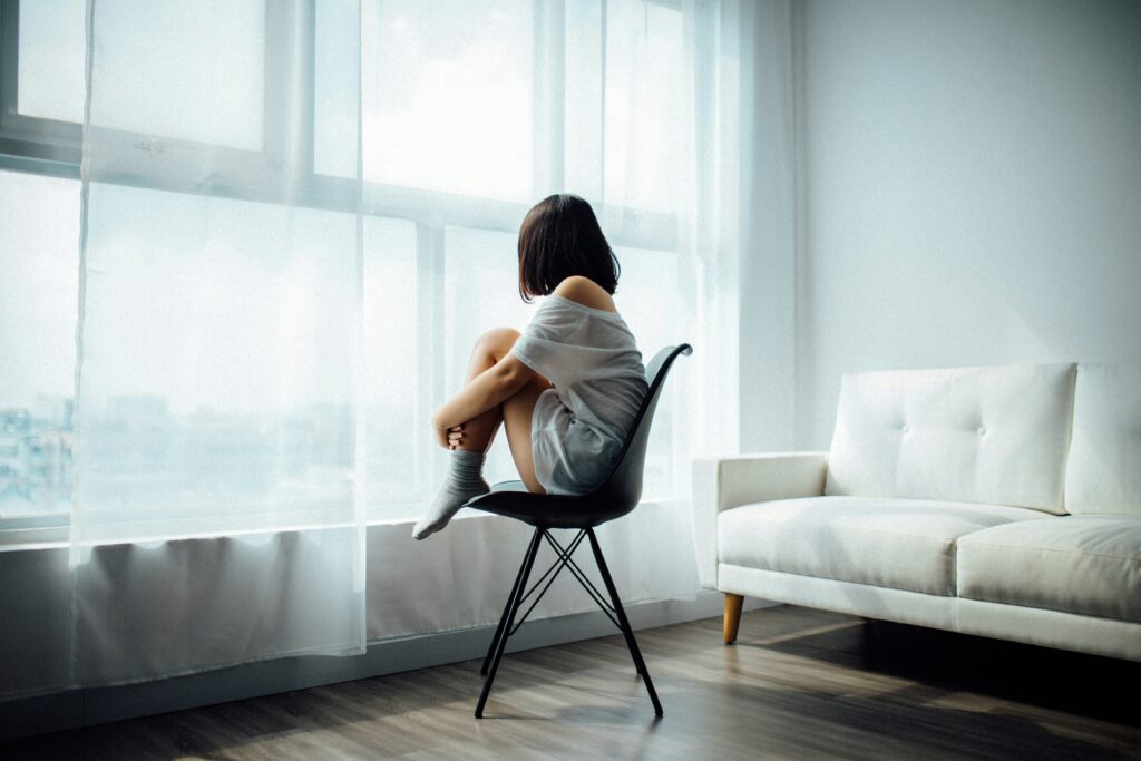  A woman sitting in a chair staring out the window, seemingly sad from symptoms of low progesterone