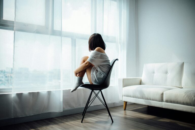 A woman sitting in a chair staring out the window, seemingly sad from symptoms of low progesterone